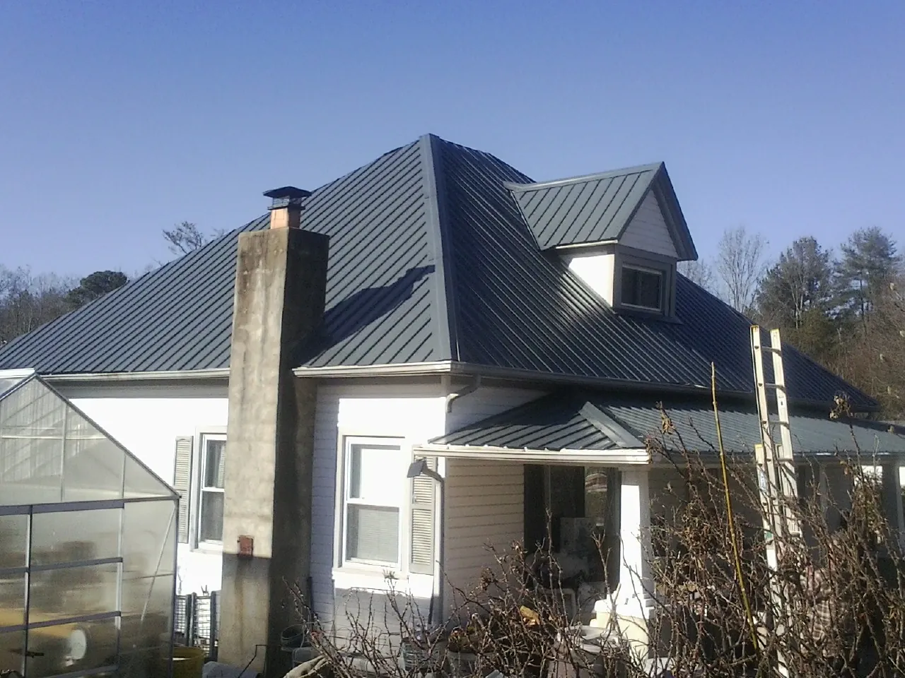 Dark blue standing seam metal roof on a white farmhouse with dormer — Slate & Tile Roof Repair by Roofing Brothers in East Islip