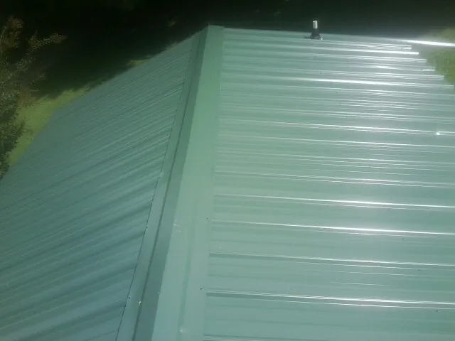 New green metal panels meeting at the ridge of a roof — Flat Roof Repair work by our crew in East Islip