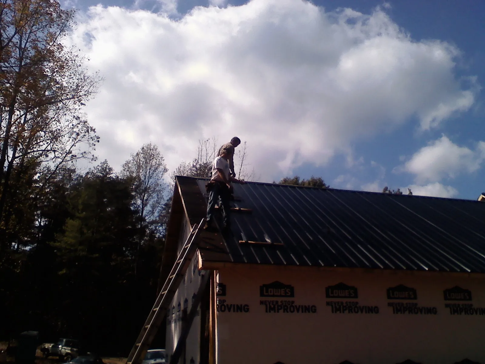 Roofer fastening dark metal panels high against a cloudy sky, from a Roof Inspection job in East Islip