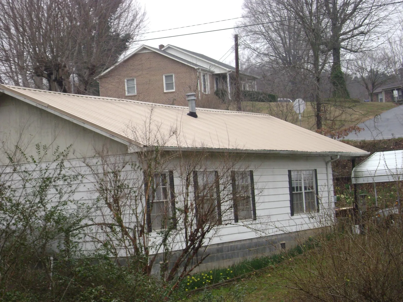 Tan metal roof on a white sided house set into a hillside — Commercial Roofing by Roofing Brothers in East Islip